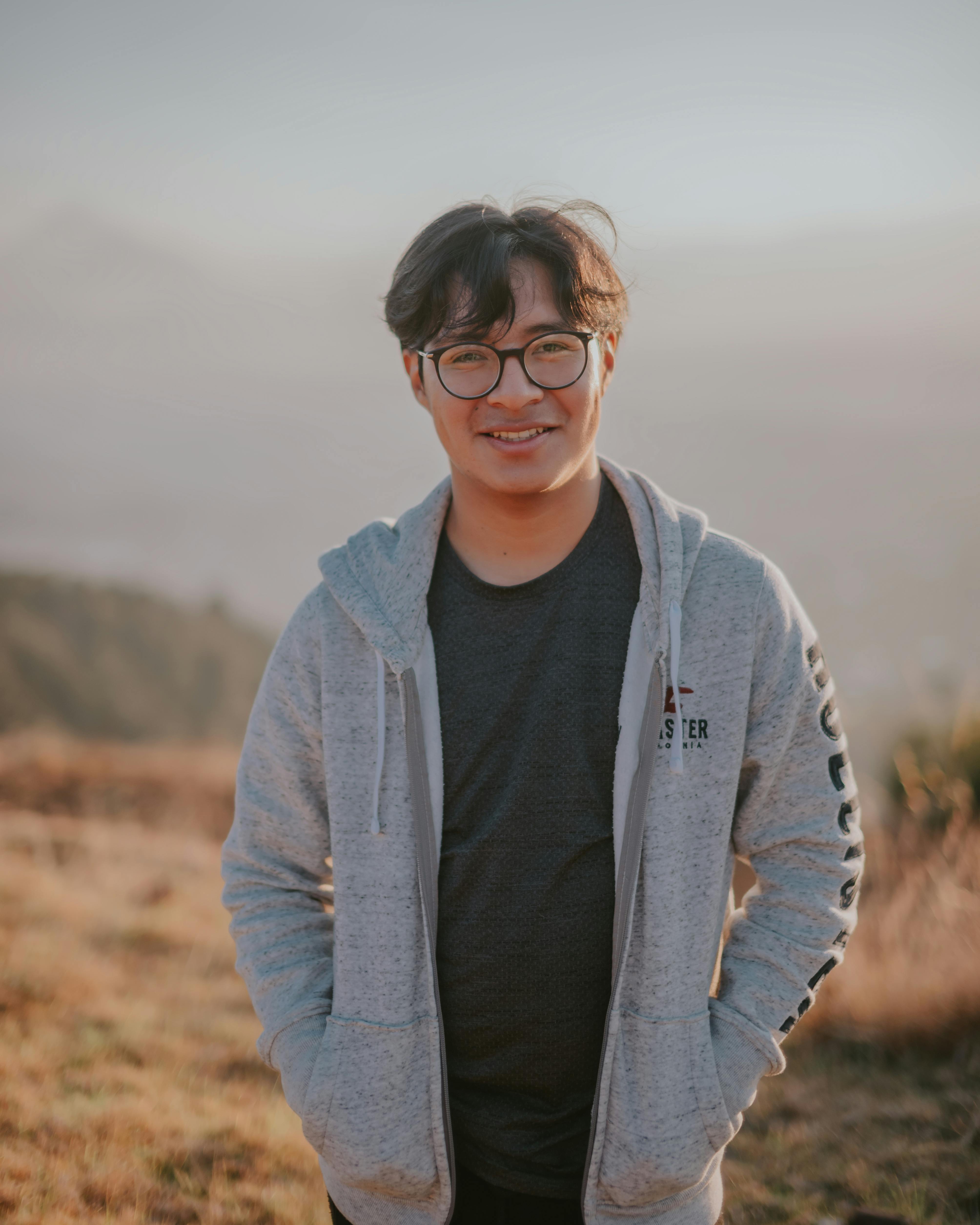 Asian man wearing eyeglasses and a casual jacket enjoying a sunny day outdoors.