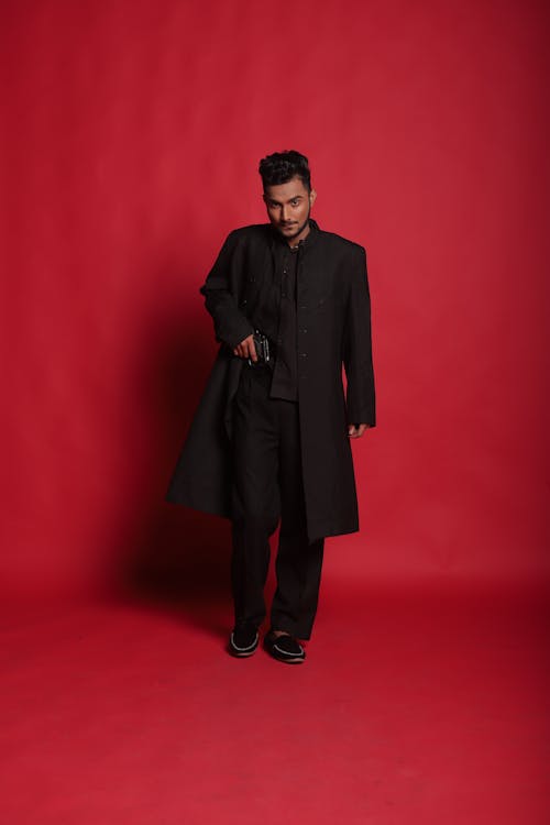 Photo of a Man in a Black Coat Standing on a Red Floor