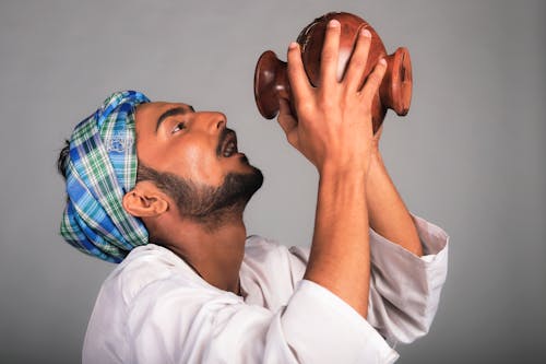 Photo of a Man Drinking From a Brown Jug