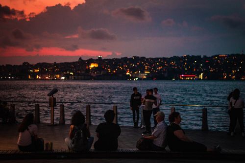 Free People enjoying a vibrant sunset by the Bosphorus with Istanbul's cityscape backdrop. Stock Photo