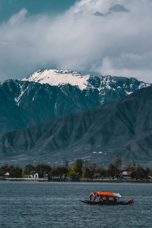 Free Peaceful scene of a snow-capped mountain and a boat on a tranquil lake under a cloudy sky. Stock Photo