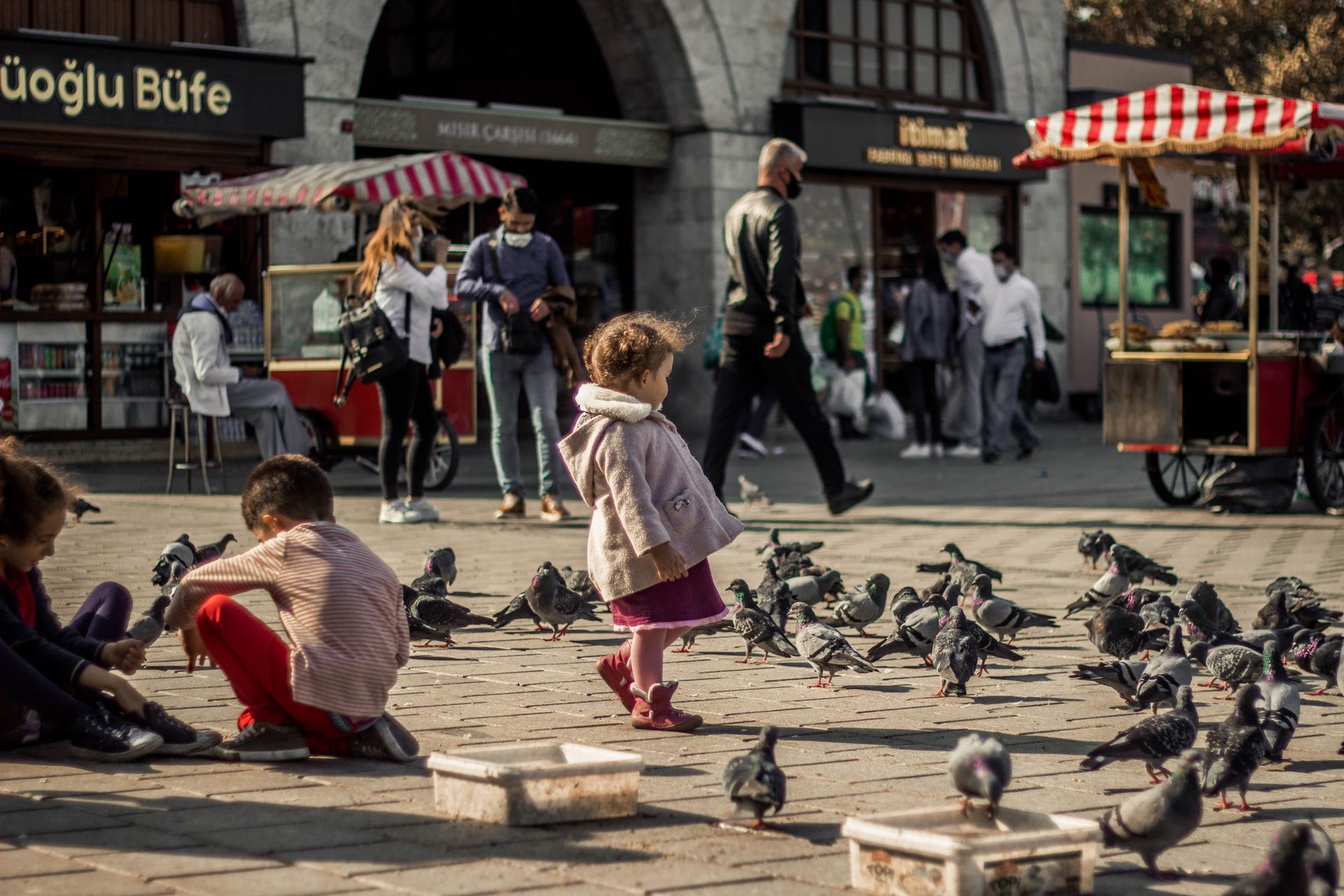 Charming scene of children interacting with pigeons in a bustling Istanbul market square.