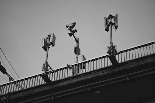 Grayscale Photo of a CCTV Camera and Solar Lights on Steel Railing