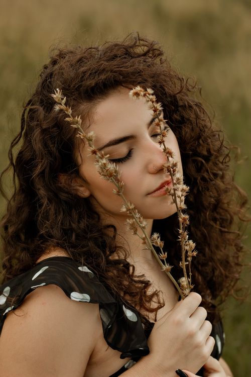 Free Close-up portrait of a brunette woman with curly hair holding flowers, eyes closed, in nature. Stock Photo