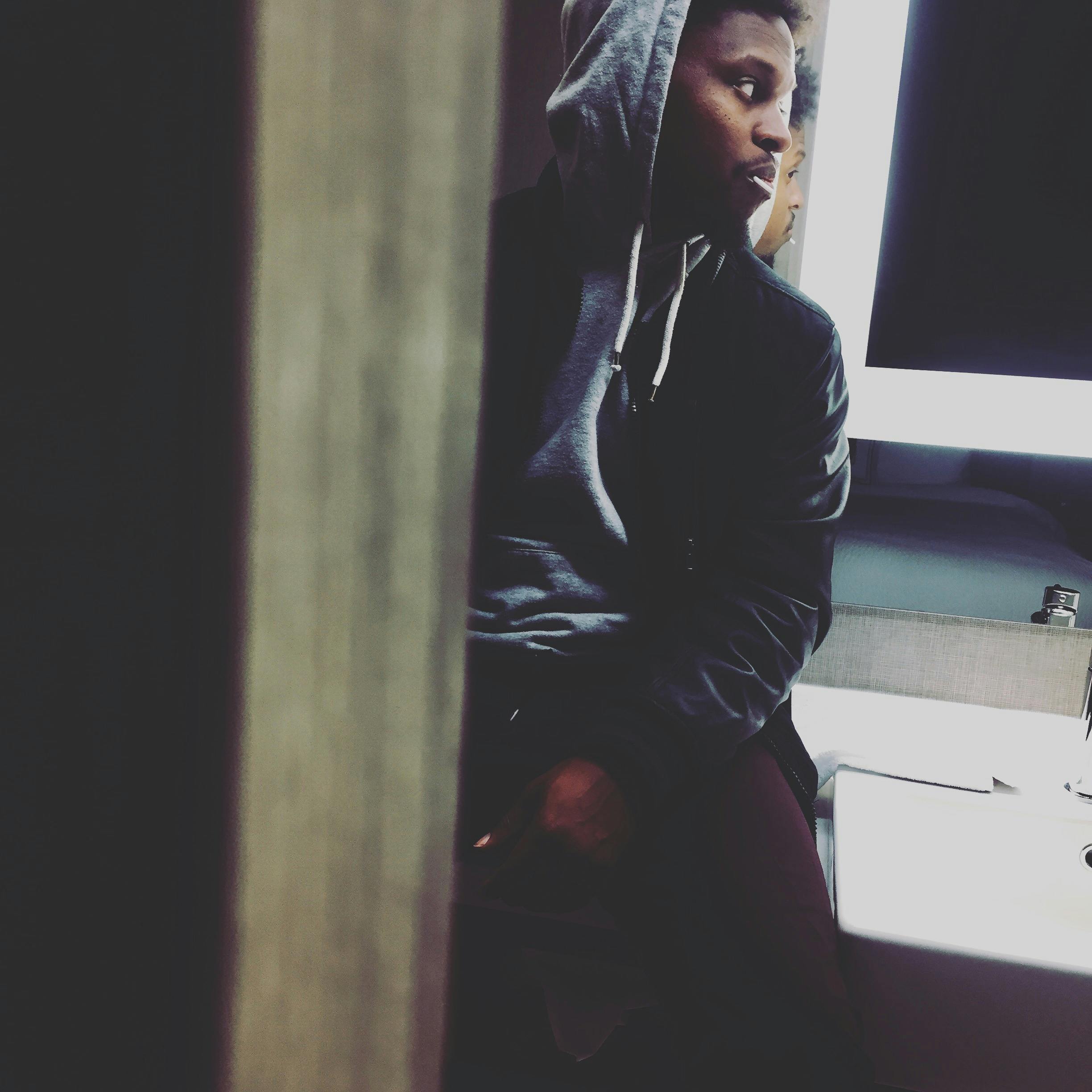 Portrait of a man in a hoodie sitting indoors with reflective lighting and a thoughtful expression.