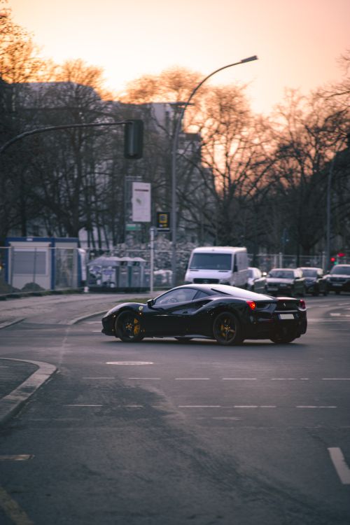 Free A sleek black Ferrari navigating city streets during sunset, showcasing urban elegance and automotive luxury. Stock Photo