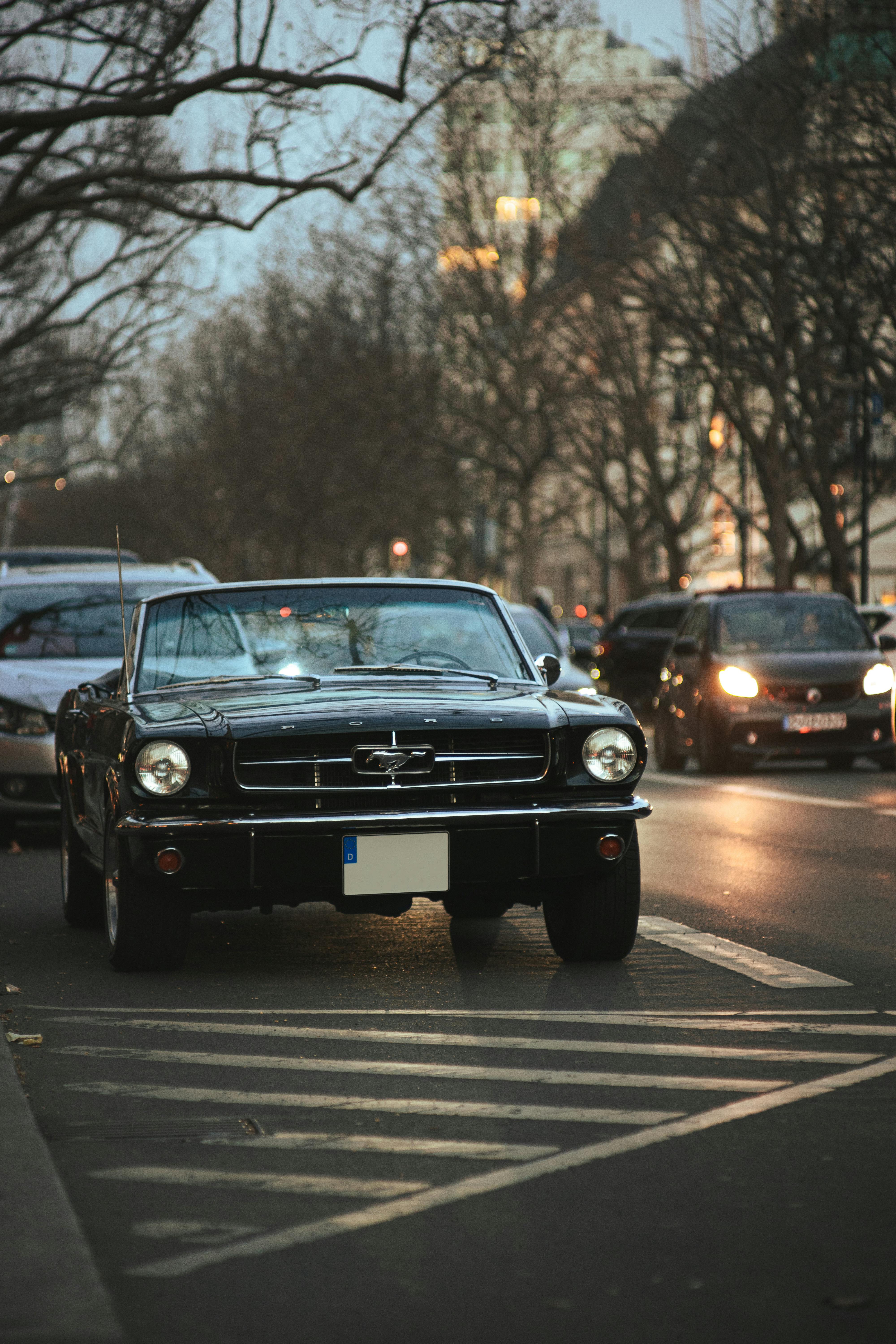 Vintage Ford Mustang convertible under city lights on a quiet road in the evening.