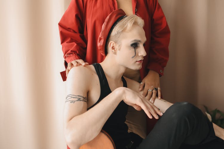 A Man In Black Tank Top With A Red Hat Sitting Beside A Person In Red Jacket