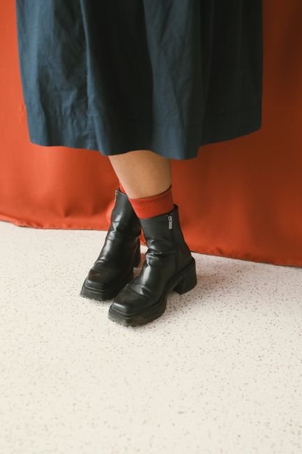 Close-up of black boots paired with red socks against a red backdrop.