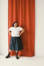Woman in White Shirt and Black Skirt Standing Beside Red Curtain