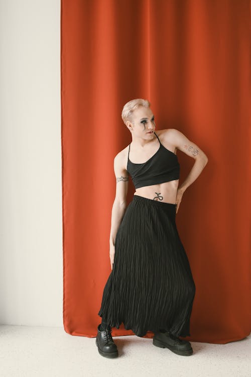 Woman in a Black Top and Skirt with Tattoos Posing in Front of a Red Curtain