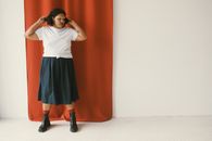 A Woman in Black Skirt and Boots Standing Near the Red Curtain with Her Hands on Her Hair