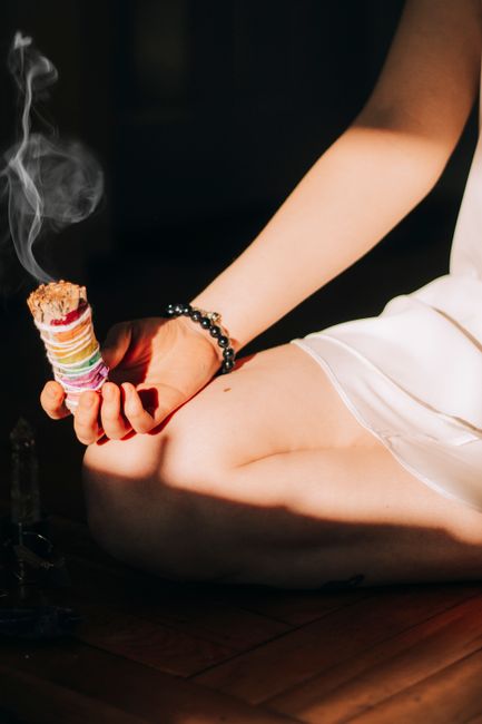 Crop anonymous female with aromatic burning smudge sticks in hand in bright daylight