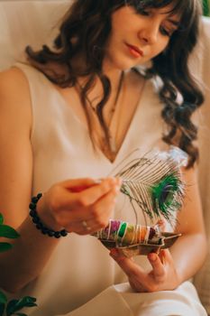 Crop delicate female with long wavy dark hair in white blouse resting with smudge sticks