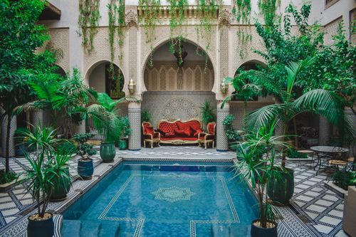 Free Elegant Moroccan courtyard featuring lush greenery and a decorative pool, perfect for a serene escape. Stock Photo