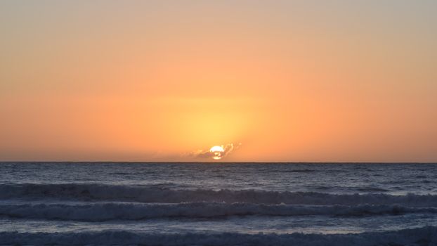 Breathtaking sunset casting orange hues over the ocean waves, creating a serene seascape.