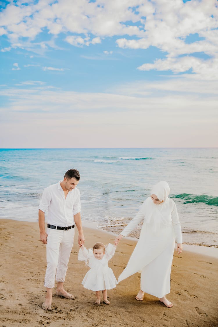 Muslim Family Walking On Sandy Beach Near Sea In Summer Time