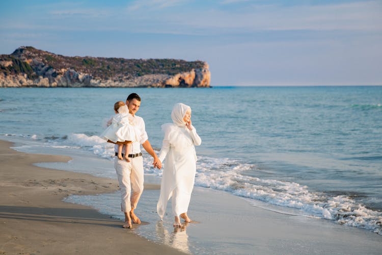 Muslim Couple Walking With Child On Sandy Beach Near Sea