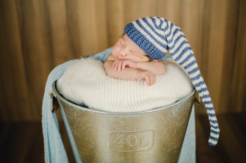 Adorable baby in nightcap sleeping in bucket