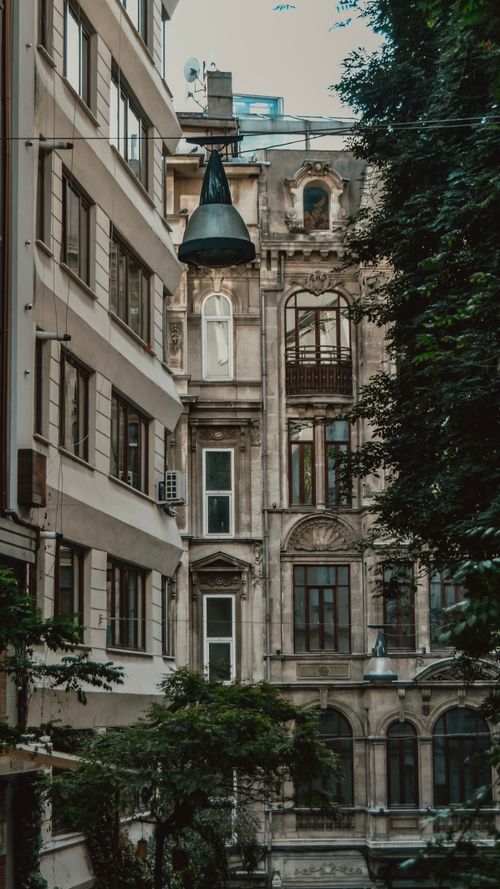 Free Vertical shot of a historic building facade with modern elements intertwined, trees and a street lamp visible. Stock Photo