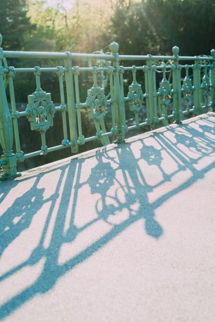 Artistic shot of a green iron bridge railing casting intricate shadows on a sunny day.