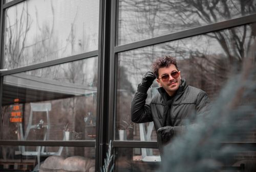 Free A man in stylish winter attire outside a building with large glass windows, exuding confidence. Stock Photo