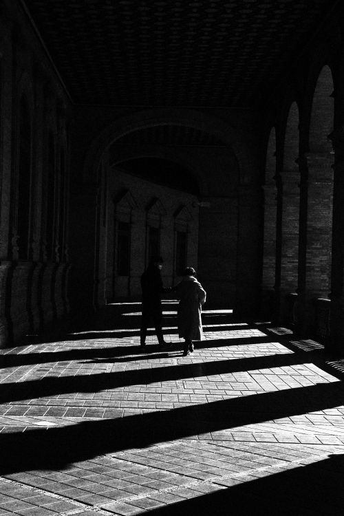 Free A dramatic silhouette of two people walking in a shadowed corridor in Seville, Spain. Stock Photo