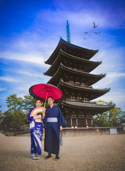 Couple in traditional Japanese clothing by a historic pagoda under a blue sky.