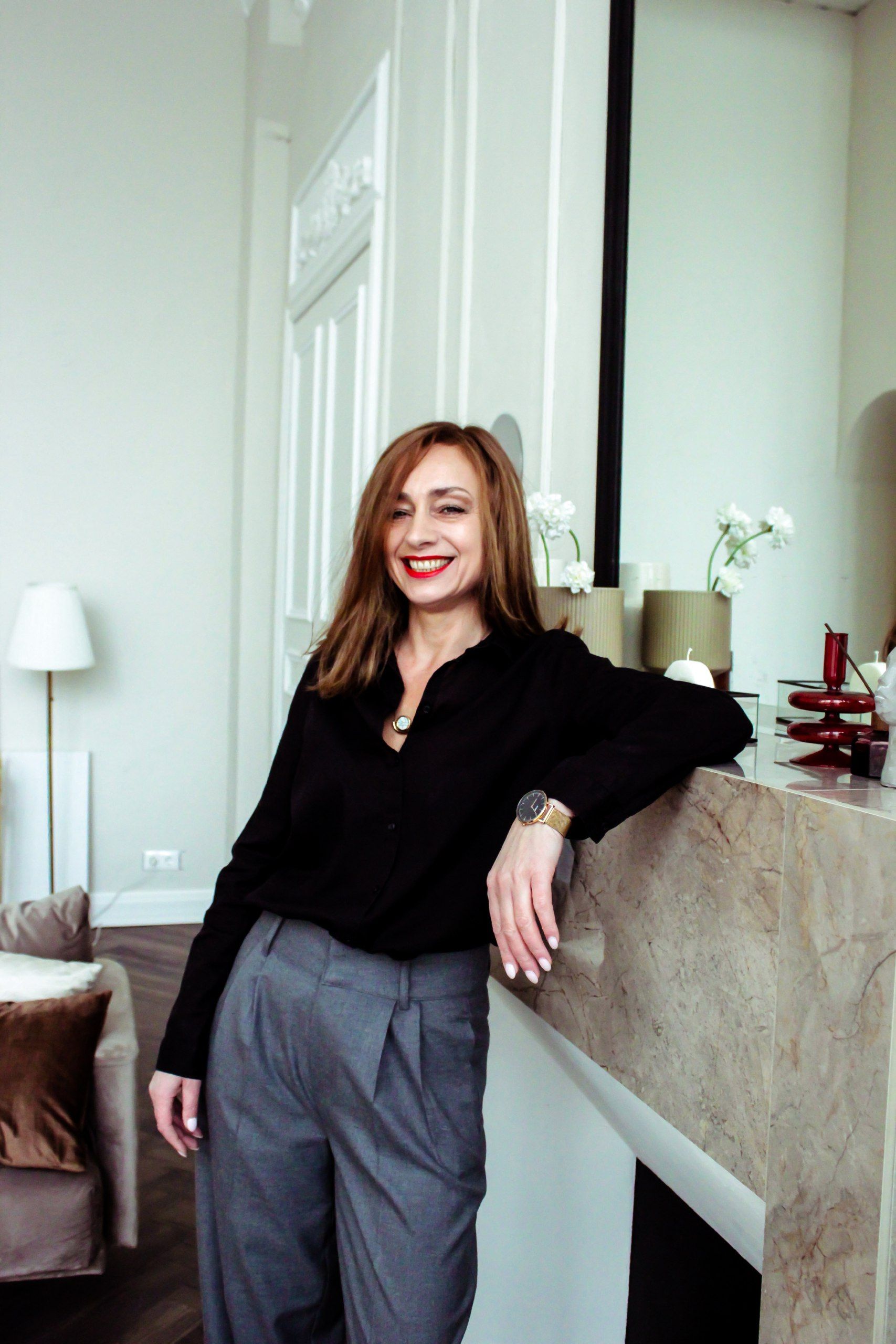 A smiling businesswoman leaning against a marble counter inside a modern office setting.