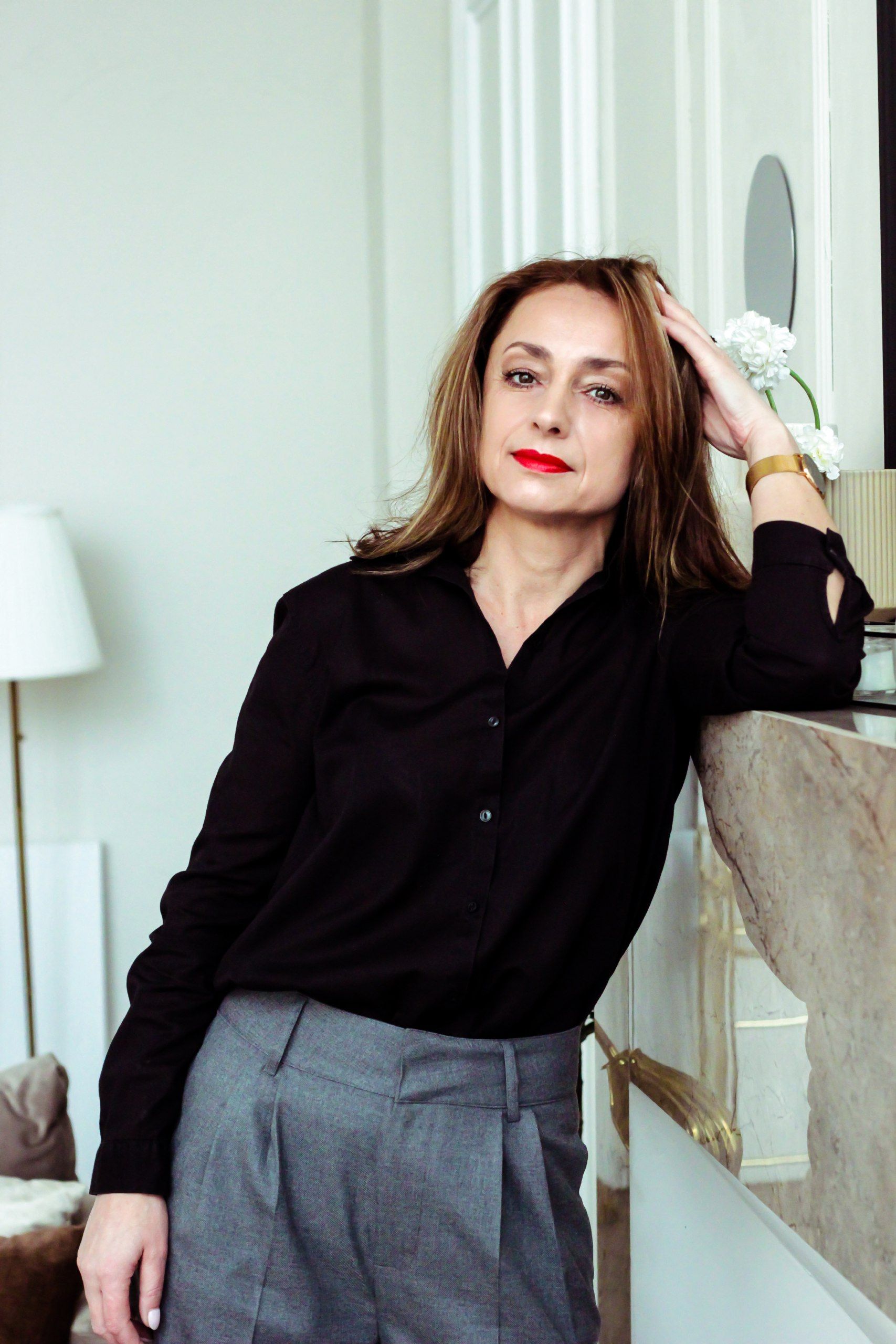 Elegant woman in black blouse and gray pants leaning on marble counter in stylish interior. Perfect for lifestyle imagery.