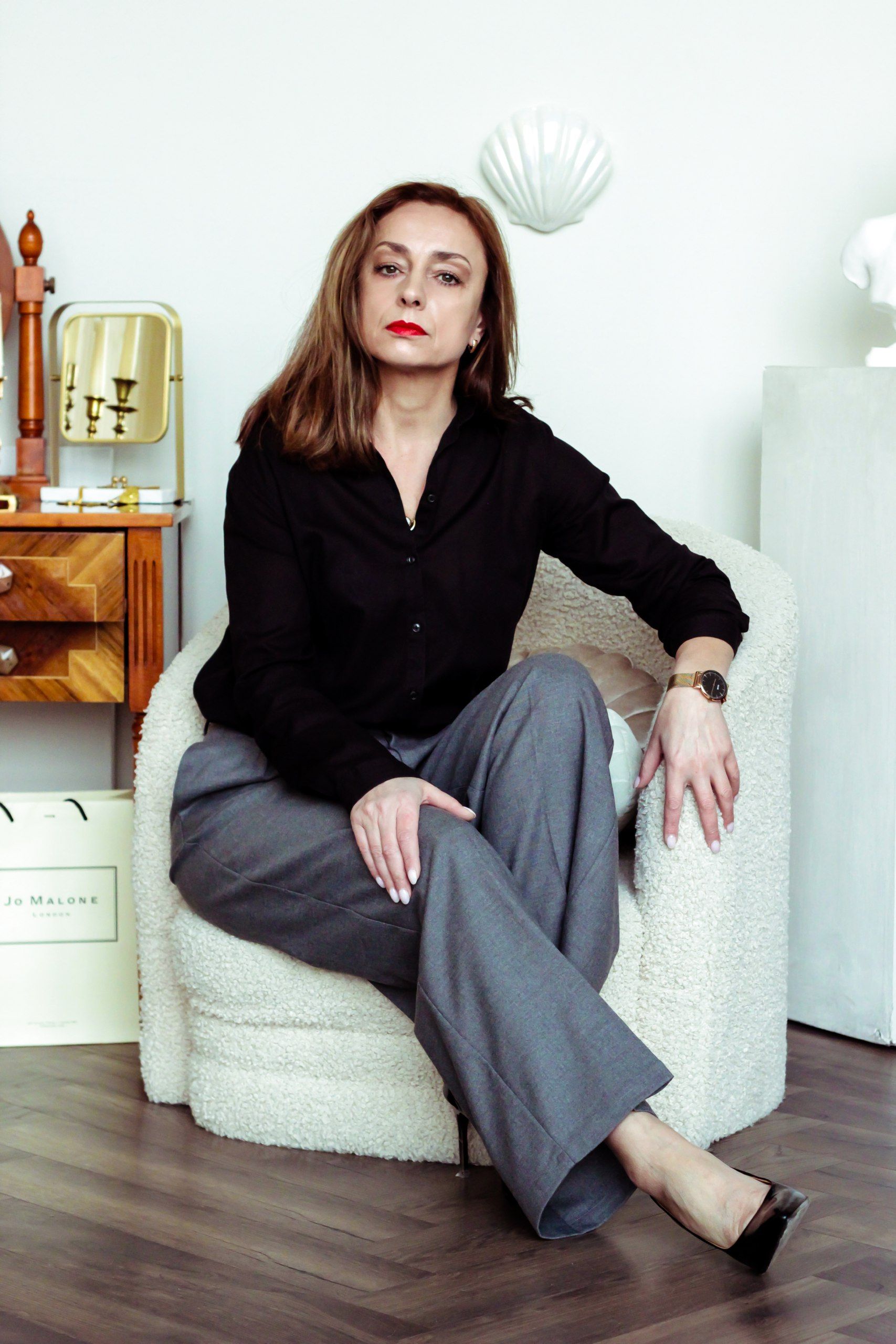 Woman in professional attire seated in a contemporary indoor setting, exuding confidence.