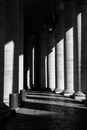 Black and white of aged stone building with columns and cobbled floor in linear shadows