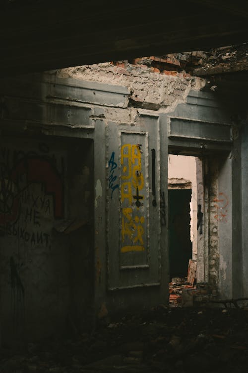 Dark room with grungy graffiti on damaged walls and shabby doorway inside desolate brick building