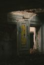 Dark room with grungy graffiti on damaged walls and shabby doorway inside desolate brick building