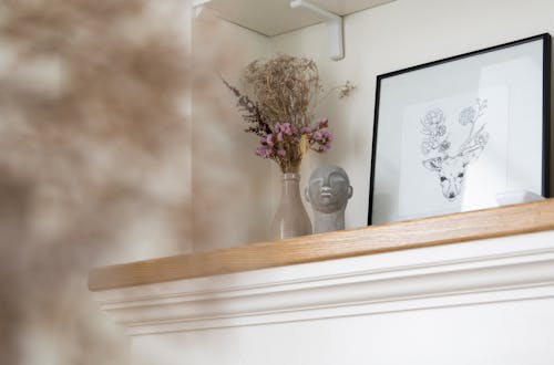 Picture of deer placed at wall on shelf near vase with decorative dried plants near figurine in light stylish apartment