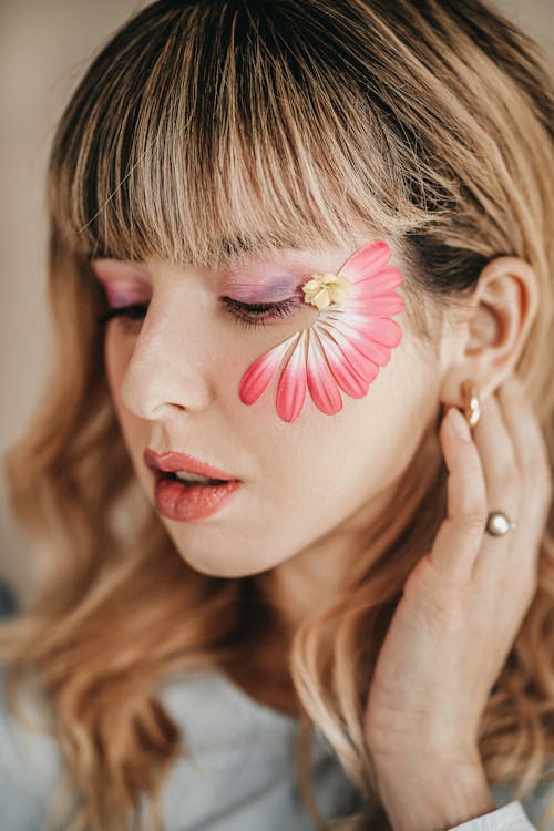 Crop tender woman with makeup and blooming flower petals with pleasant aroma on face looking down