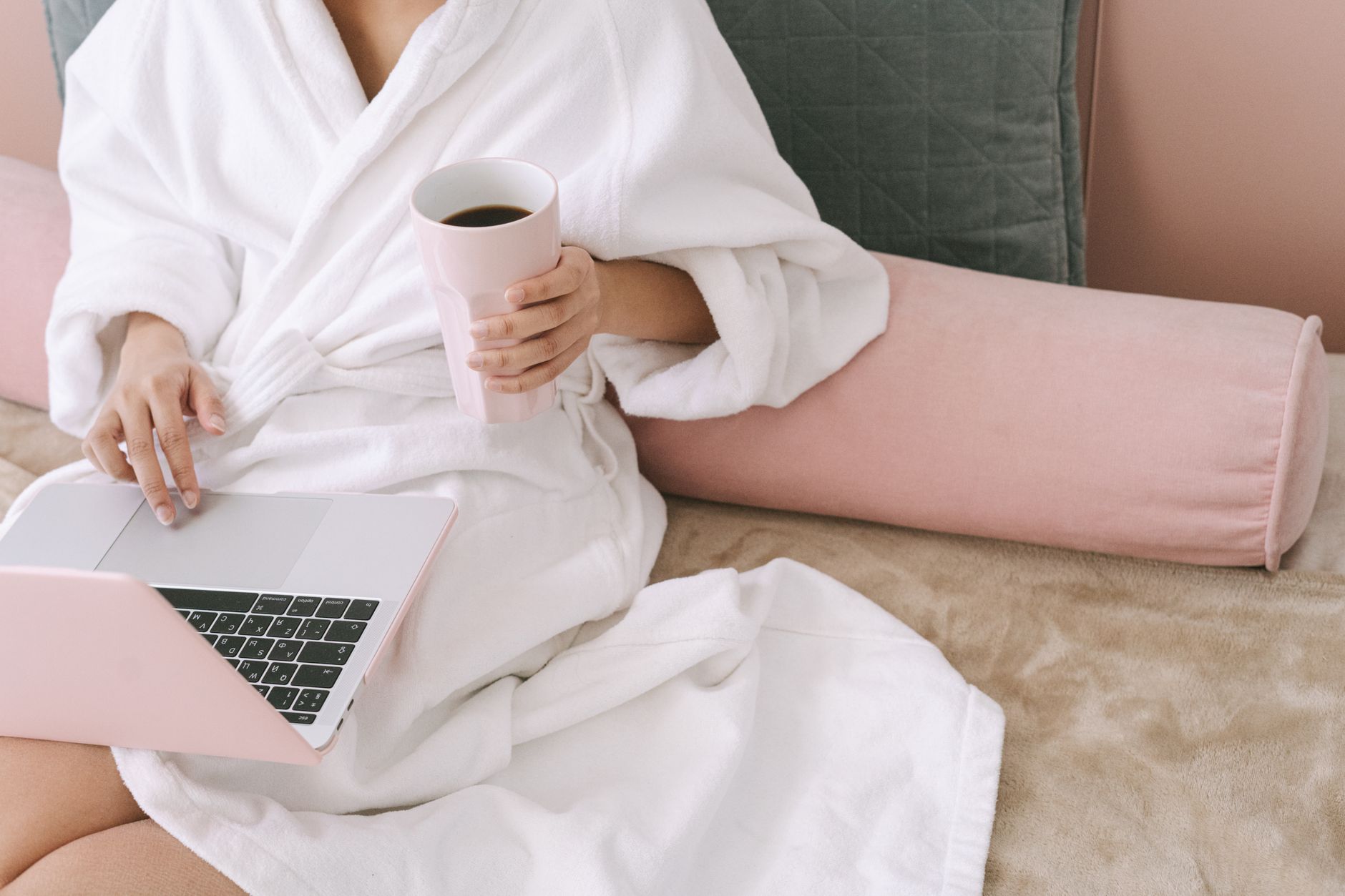 Woman in bathrobe working on a laptop while enjoying coffee, sitting comfortably indoors.