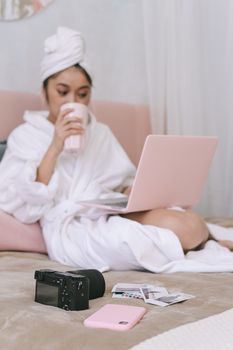 A woman in a bathrobe uses a laptop and enjoys a drink, creating a cozy and relaxing bedroom atmosphere.
