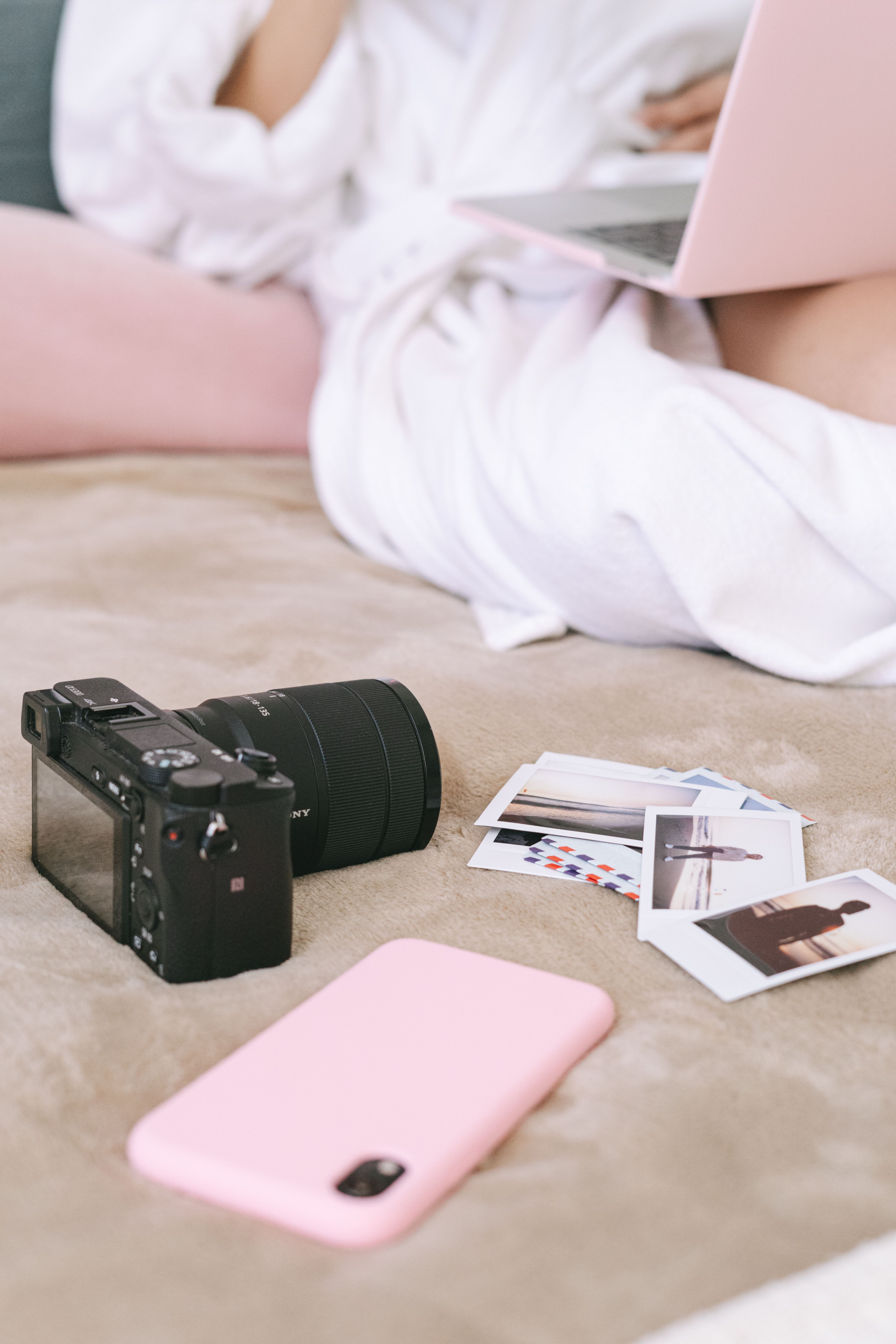 A cozy scene featuring a digital camera, photos, and a laptop on a bed.