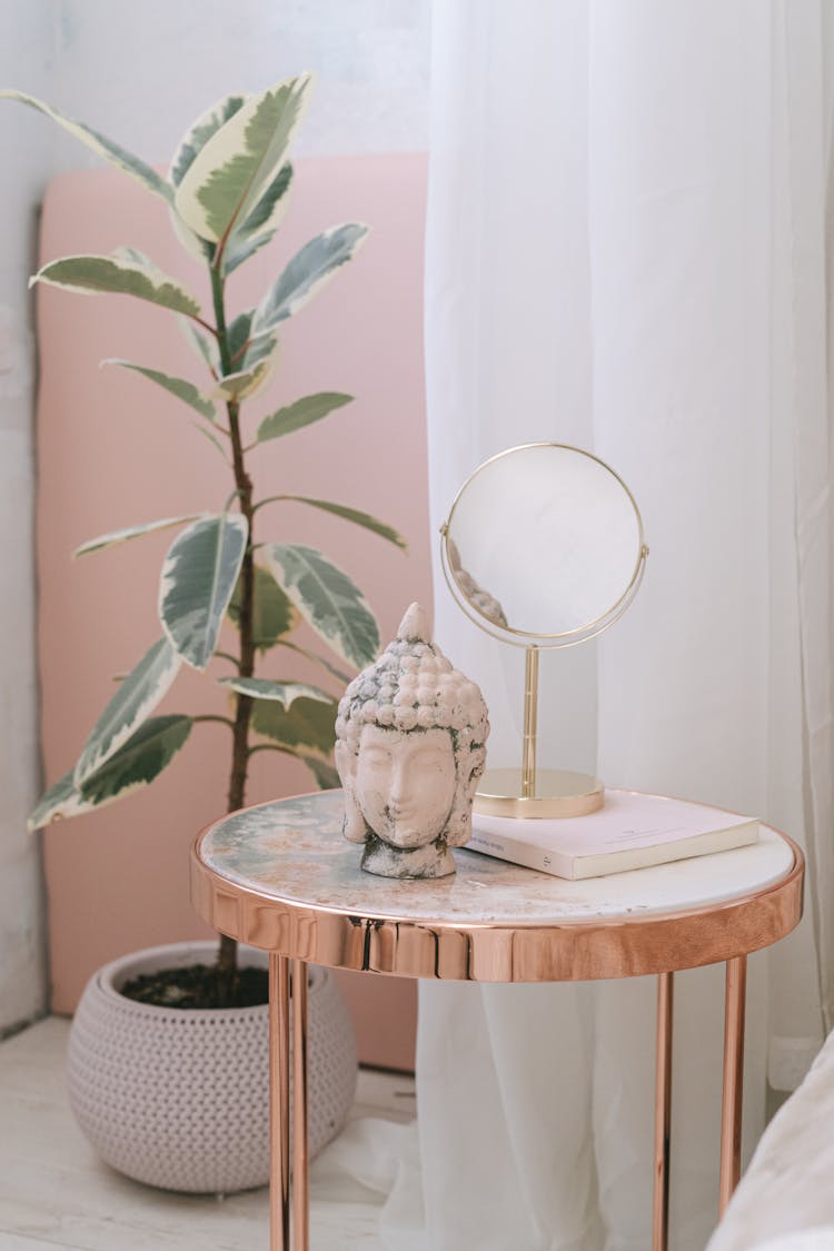 A Buddha Head And A Mirror On A Side Table