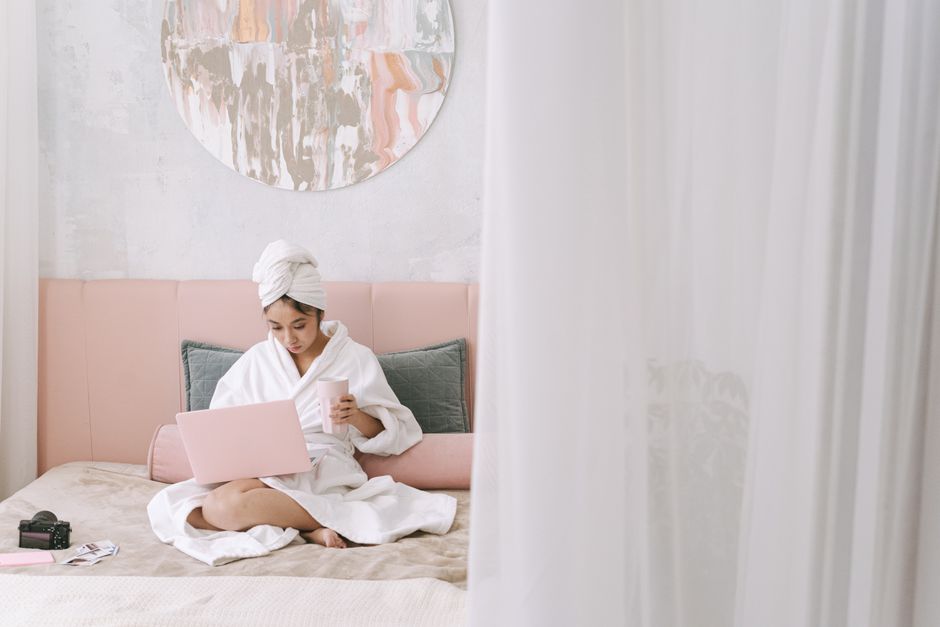 An Asian woman in a bathrobe using a laptop on her bed, exuding a cozy morning vibe.