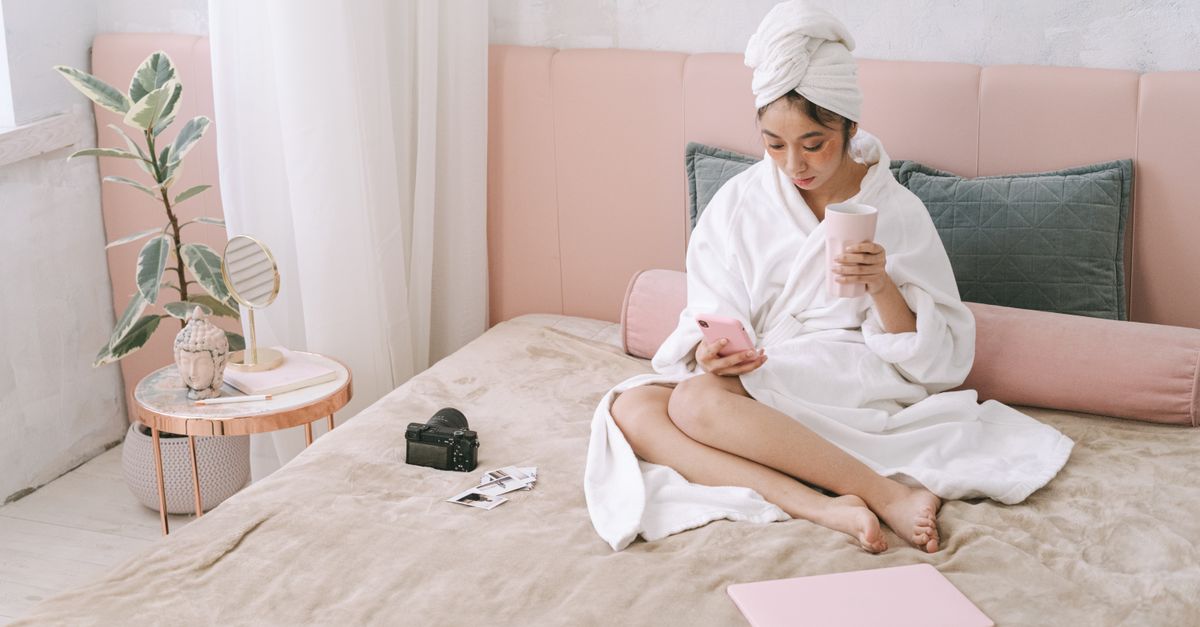 person placing smartphone on bathroom counter while holding a glass of water in a sunlit bedroom