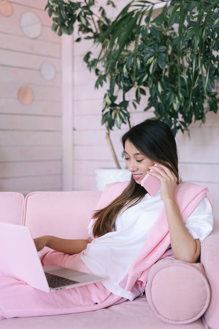 A Woman In White Shirt Sitting On The Couch While Talking On The Phone