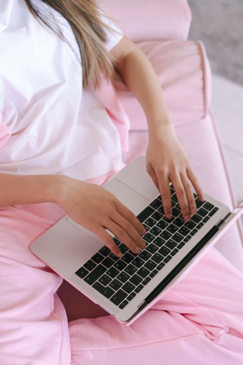 Free A young woman in pink pants works on her laptop from a cozy home setting. Perfect representation of remote work lifestyle. Stock Photo