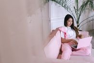 Woman Sitting on Pink Sofa Using a Laptop