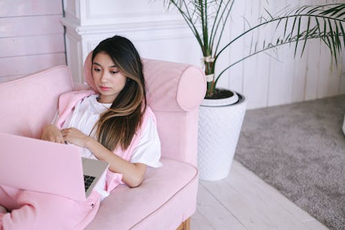 Free Woman in Pink Shirt Sitting on Sofa Using Macbook Stock Photo