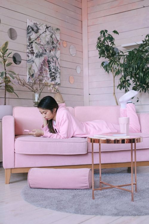 Free Young woman relaxing on a pink sofa using her smartphone, surrounded by plants and decor. Stock Photo