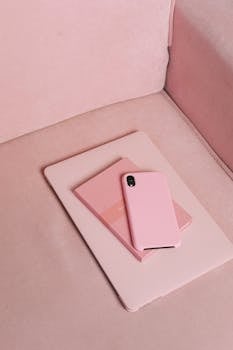 A pink smartphone and matching notebook on a pastel pink couch, showcasing a modern aesthetic.