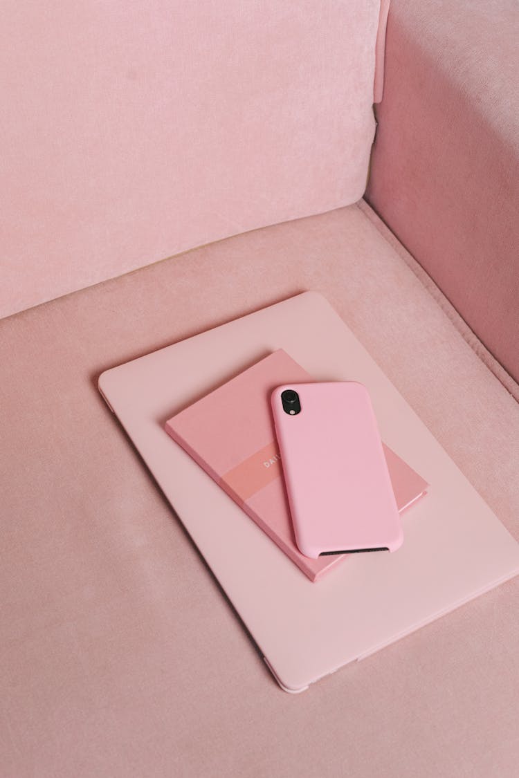 A Pink Smartphone And Notebook On Top Of A Tablet