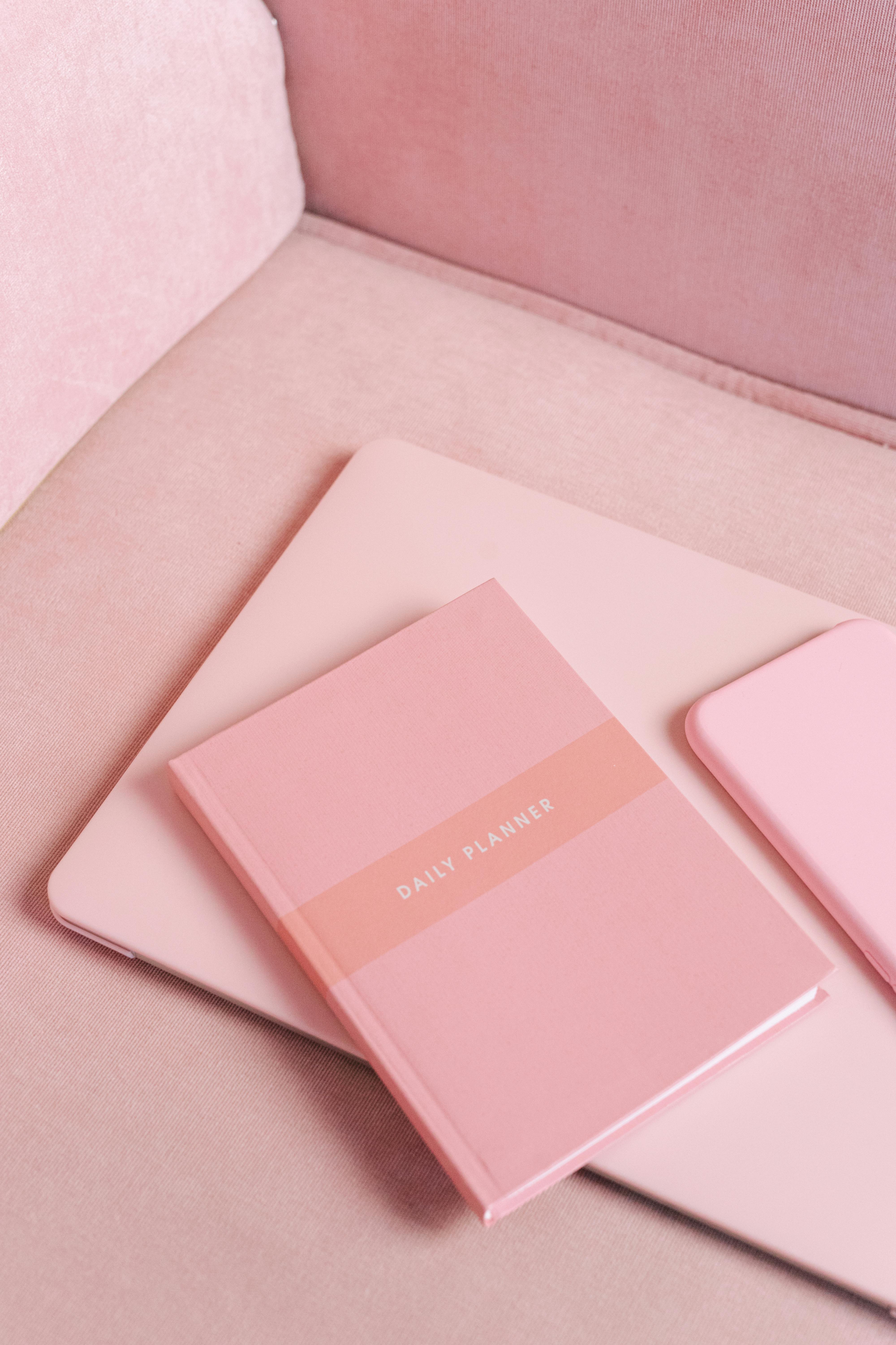 A pink-themed productivity setup featuring a daily planner, laptop, and a smartphone.